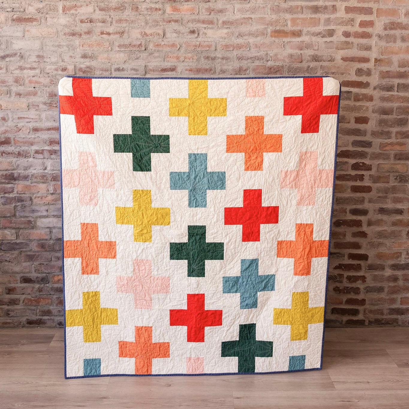 Colorful quilt with cross pattern against a brick wall