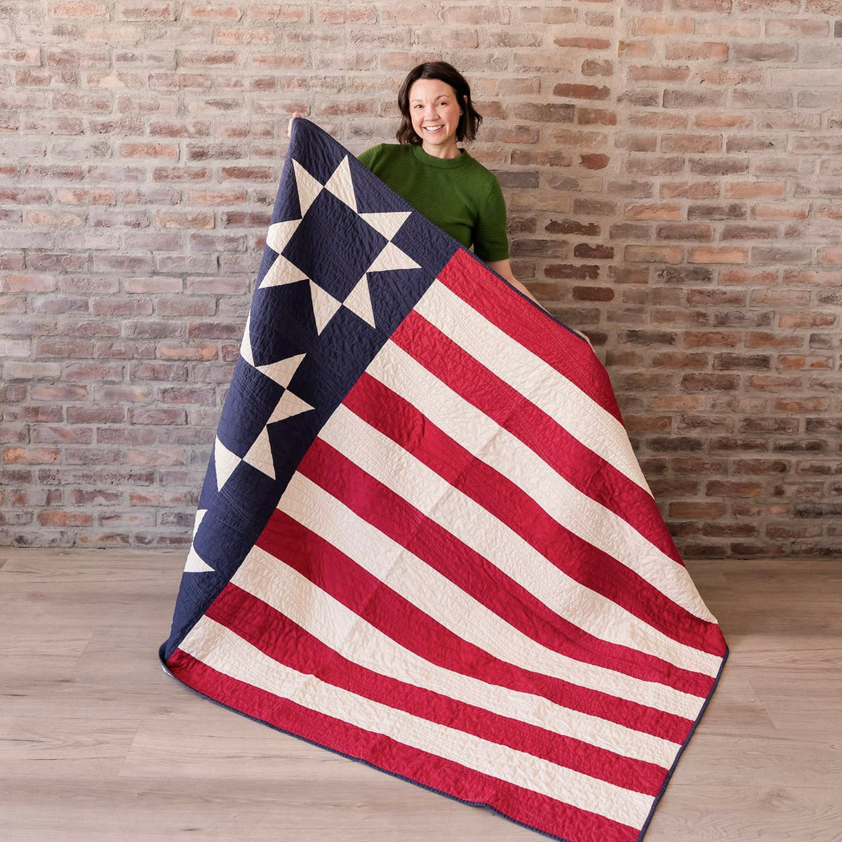 Person holding a large American flag quilt against a brick wall.