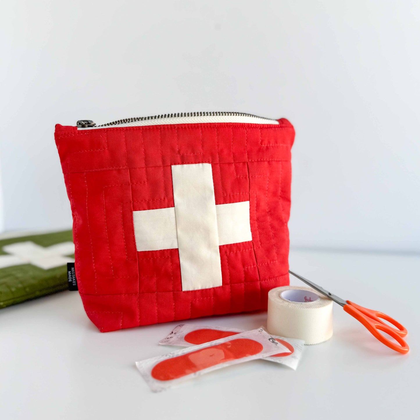 Red first aid kit with a white cross, band-aids, tape, and scissors on a white background