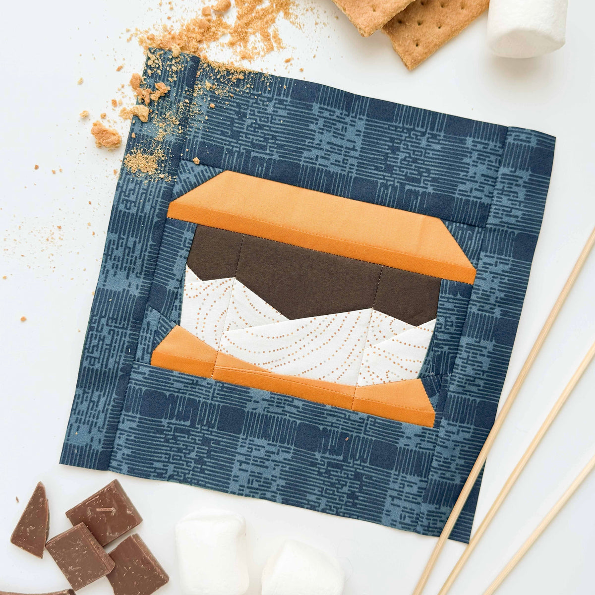 S'mores-themed quilt block with graham crackers, chocolate, and marshmallows on a white background.