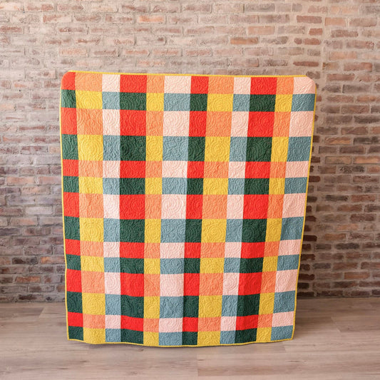 Multicolored checkered blanket on a wooden floor against a brick wall.