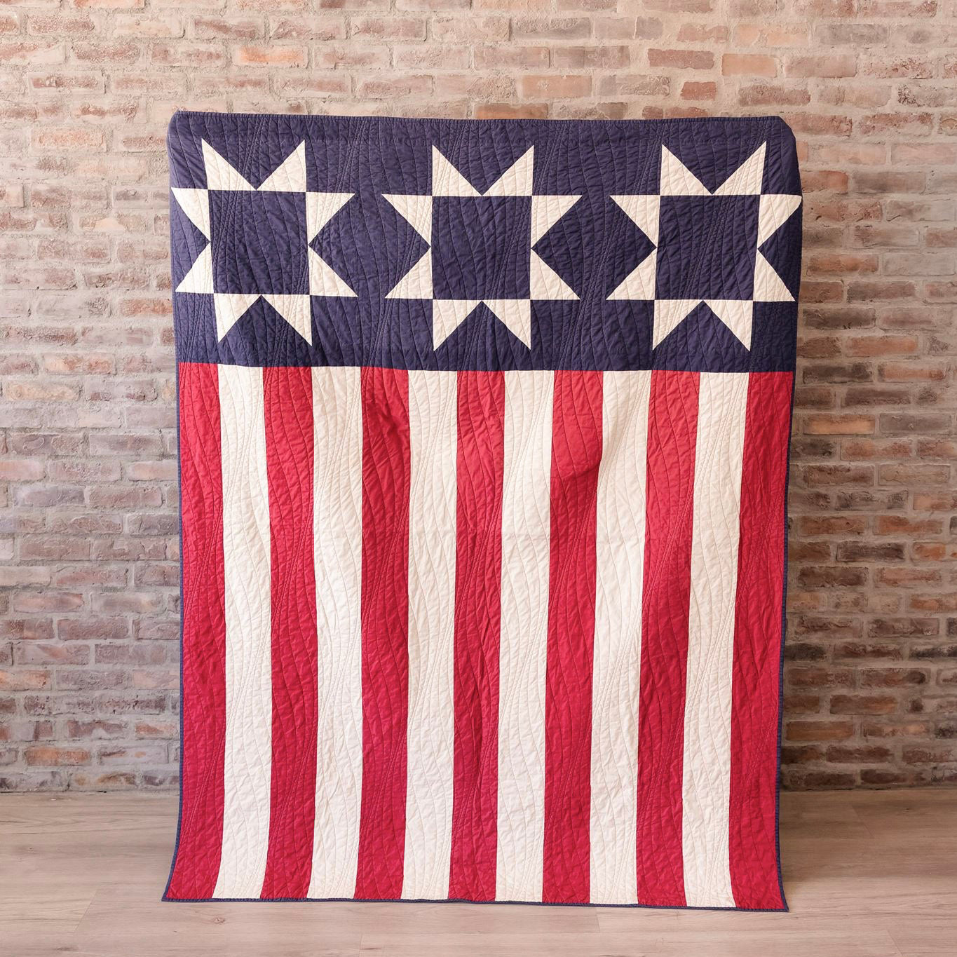 American flag quilt draped over a chair against a brick wall.