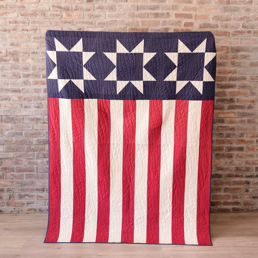American flag quilt draped over a chair against a brick wall.