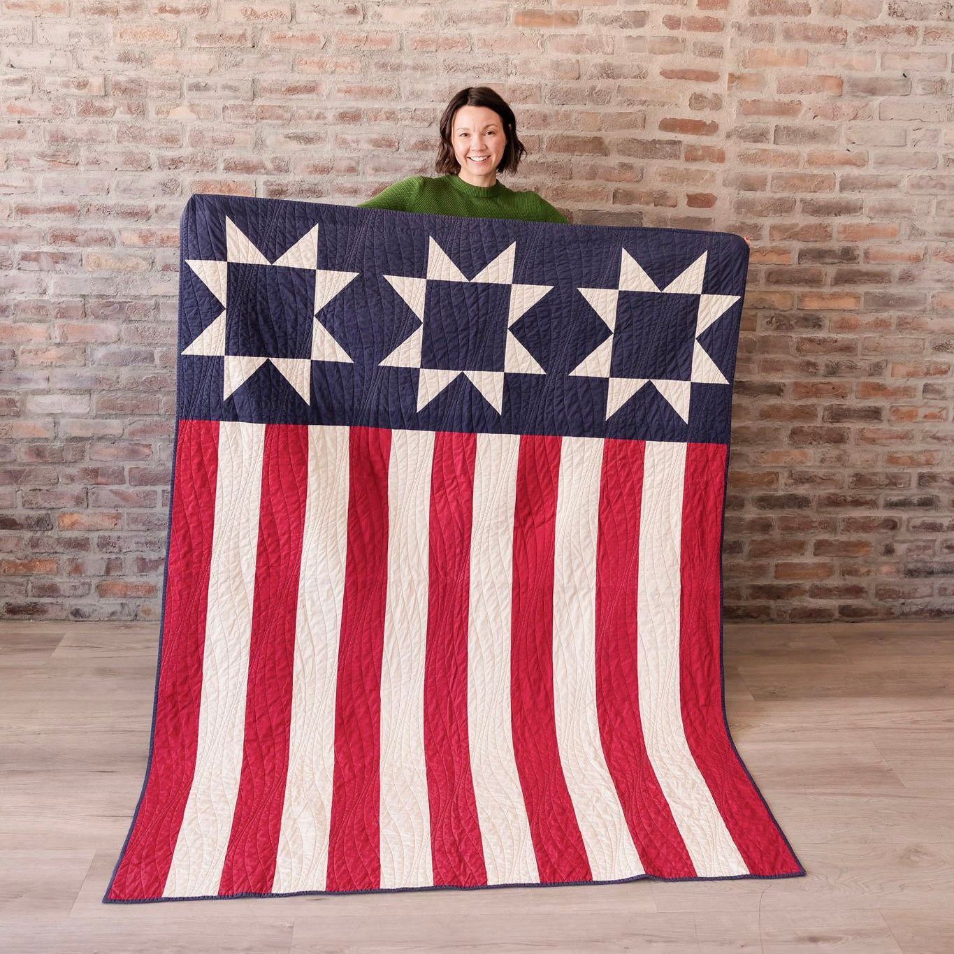 Person holding a large American flag quilt against a brick wall.