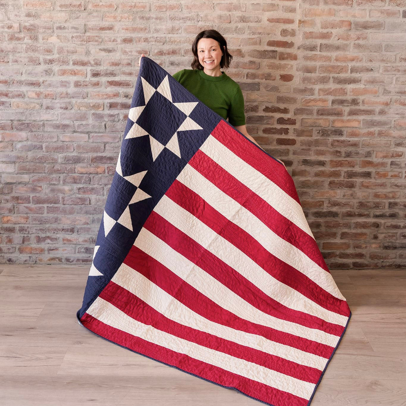 Person holding a large American flag quilt against a brick wall.