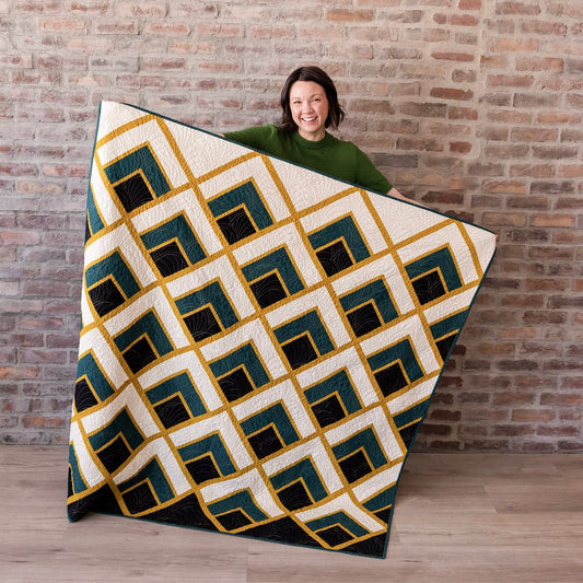 Person holding a geometric patterned blanket against a brick wall