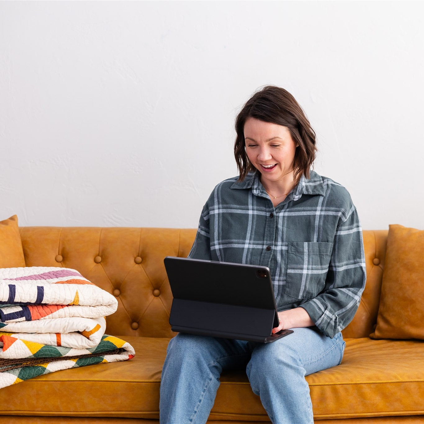 Person sitting on a brown couch using a laptop with a colorful blanket beside them.