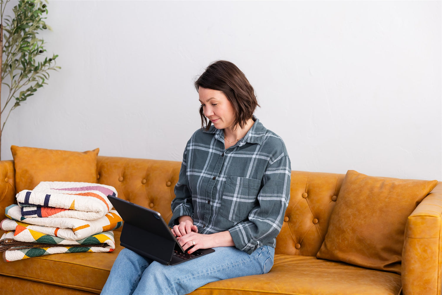 Woman using a laptop on an orange couch with colorful blankets