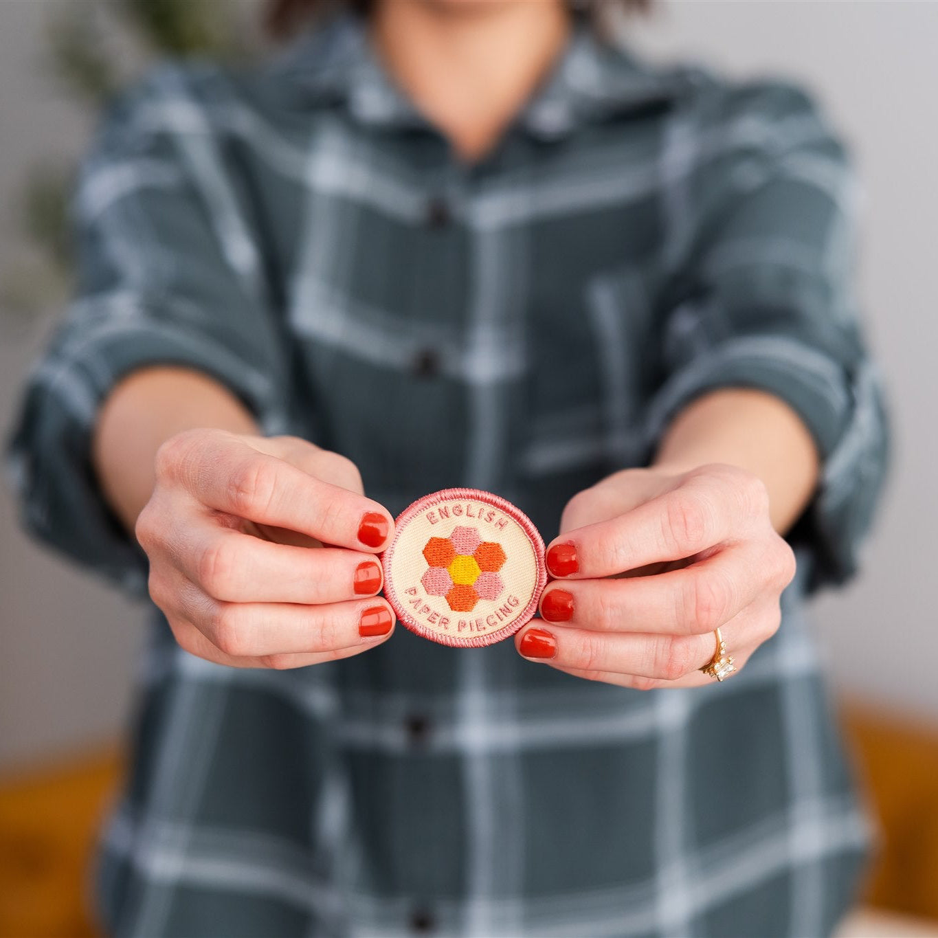 Person holding a round pink object with a logo, wearing a plaid shirt indoors.