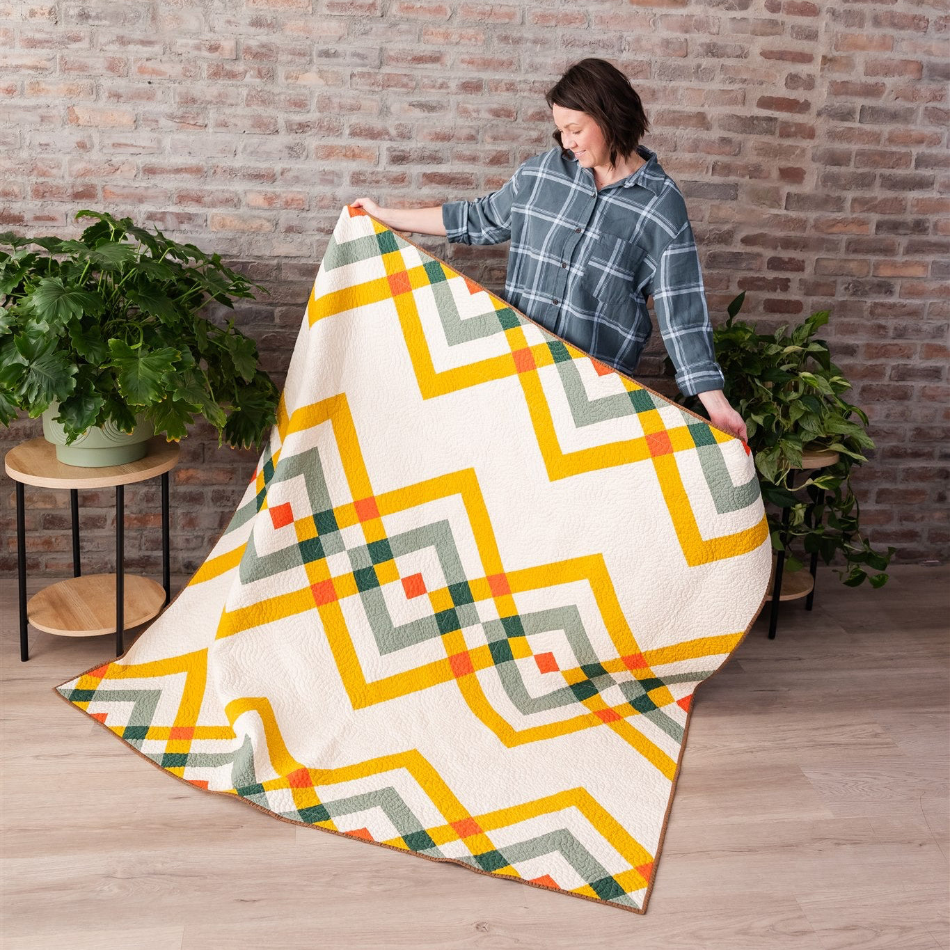 Person holding a colorful geometric-patterned blanket against a brick wall.
