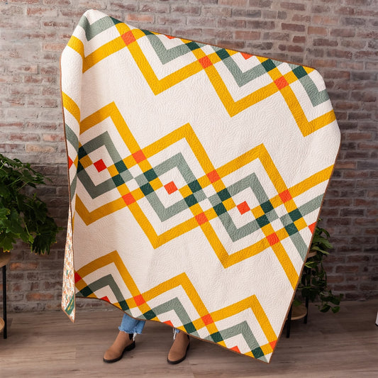 Person holding a colorful geometric-patterned blanket against a brick wall.