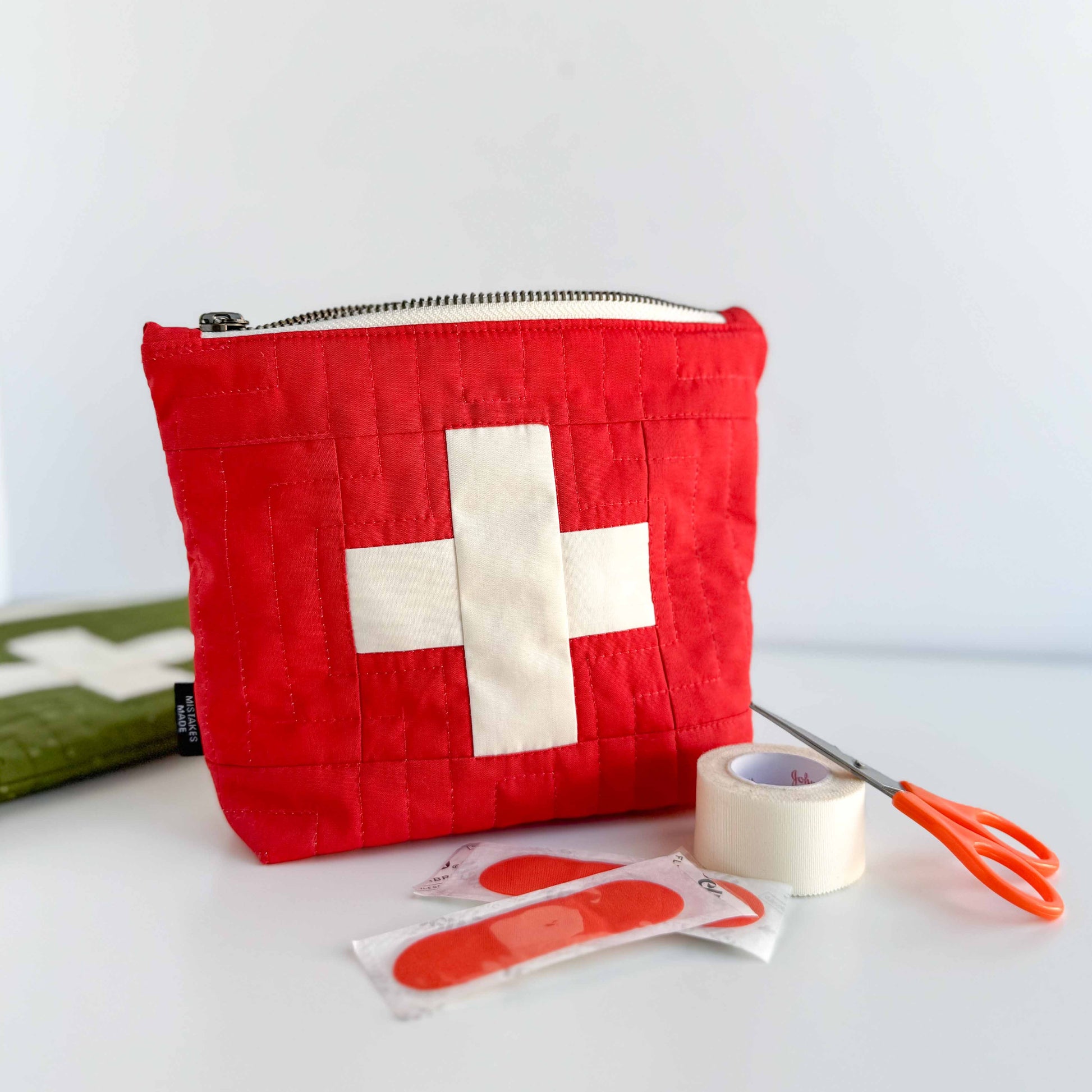 Red first aid kit with a white cross, band-aids, tape, and scissors on a white background
