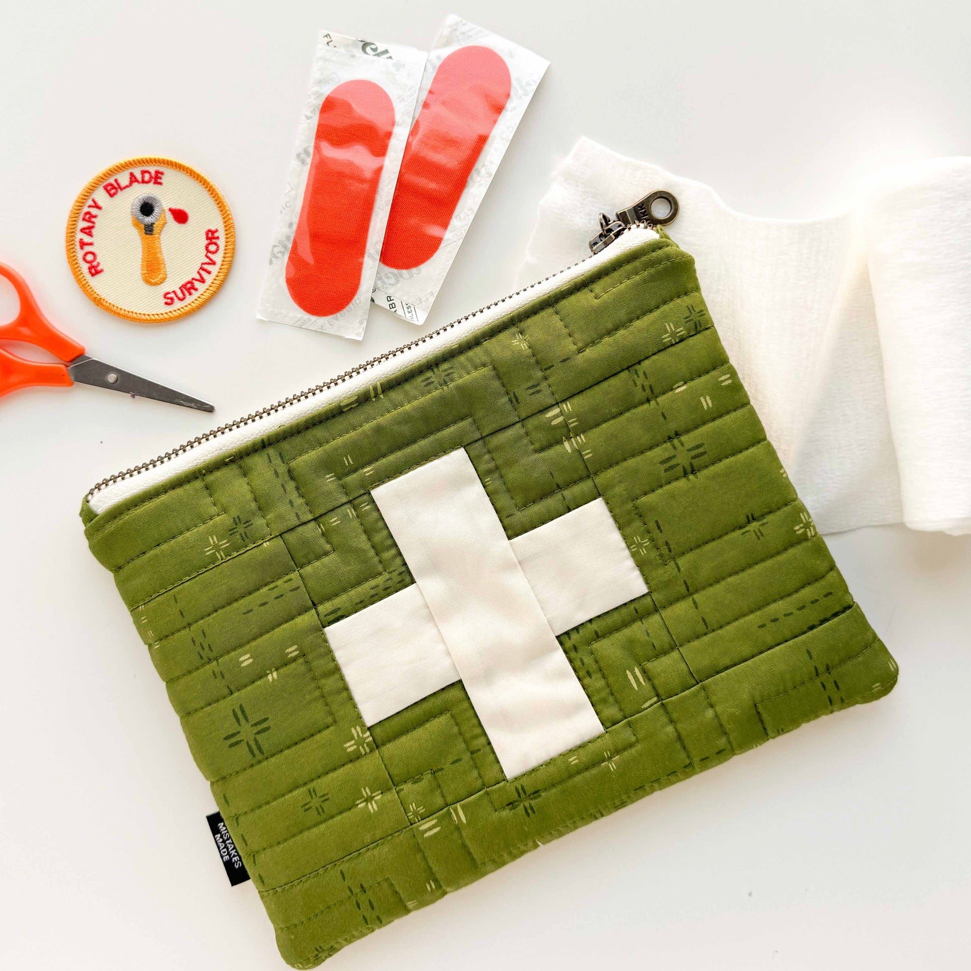 Green pouch with white cross, scissors, and band-aids on a light background