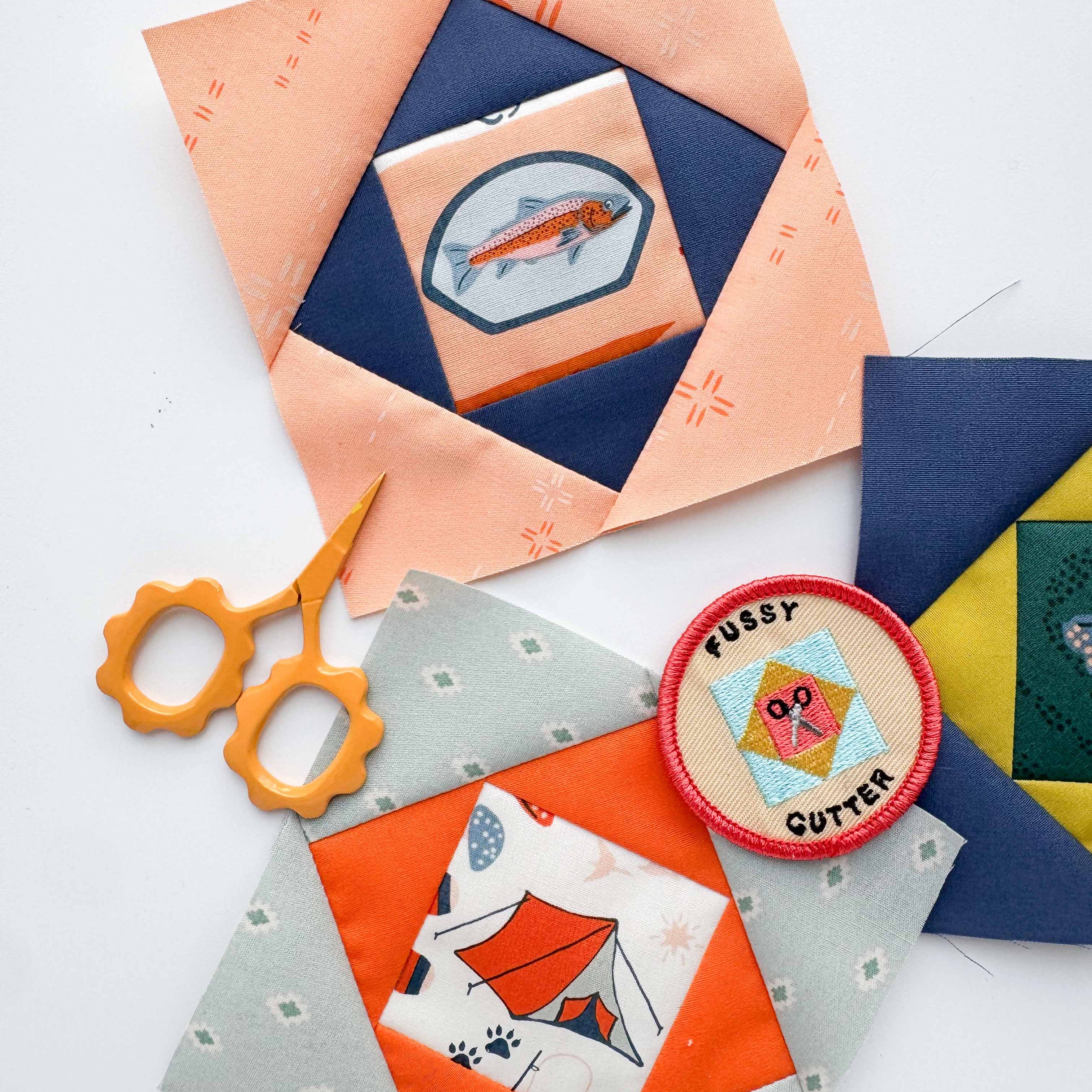 Embroidered patches on fabric blocks with a pair of scissors on a white background